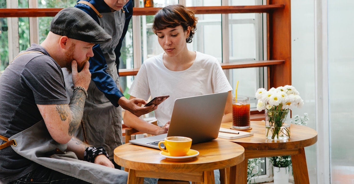 Employees of a cafe work together on laptop and smartphone