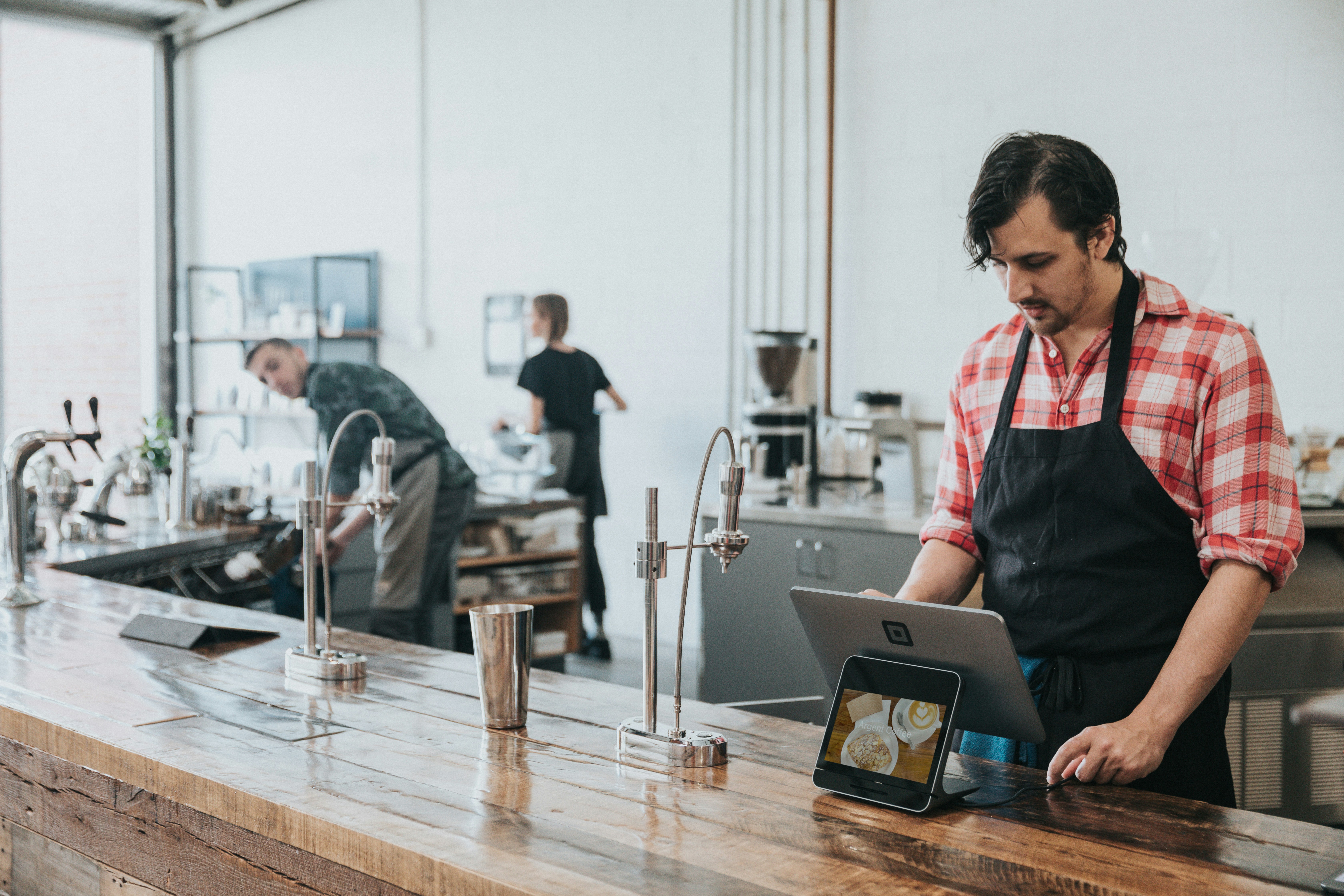 An employee operates a tablet at the counter in a café