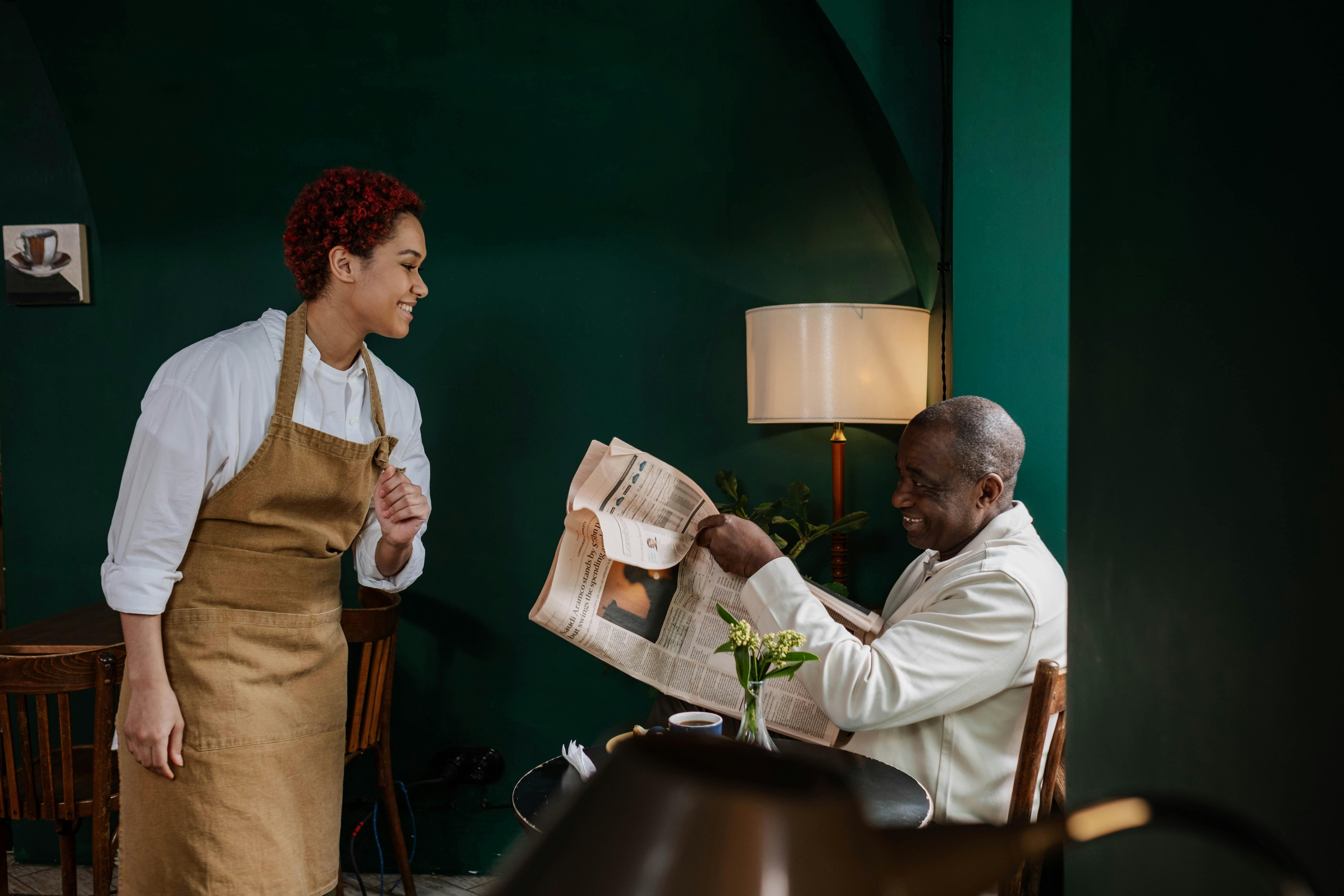 servicekraft lacht mit einem gast, der zeitung liest