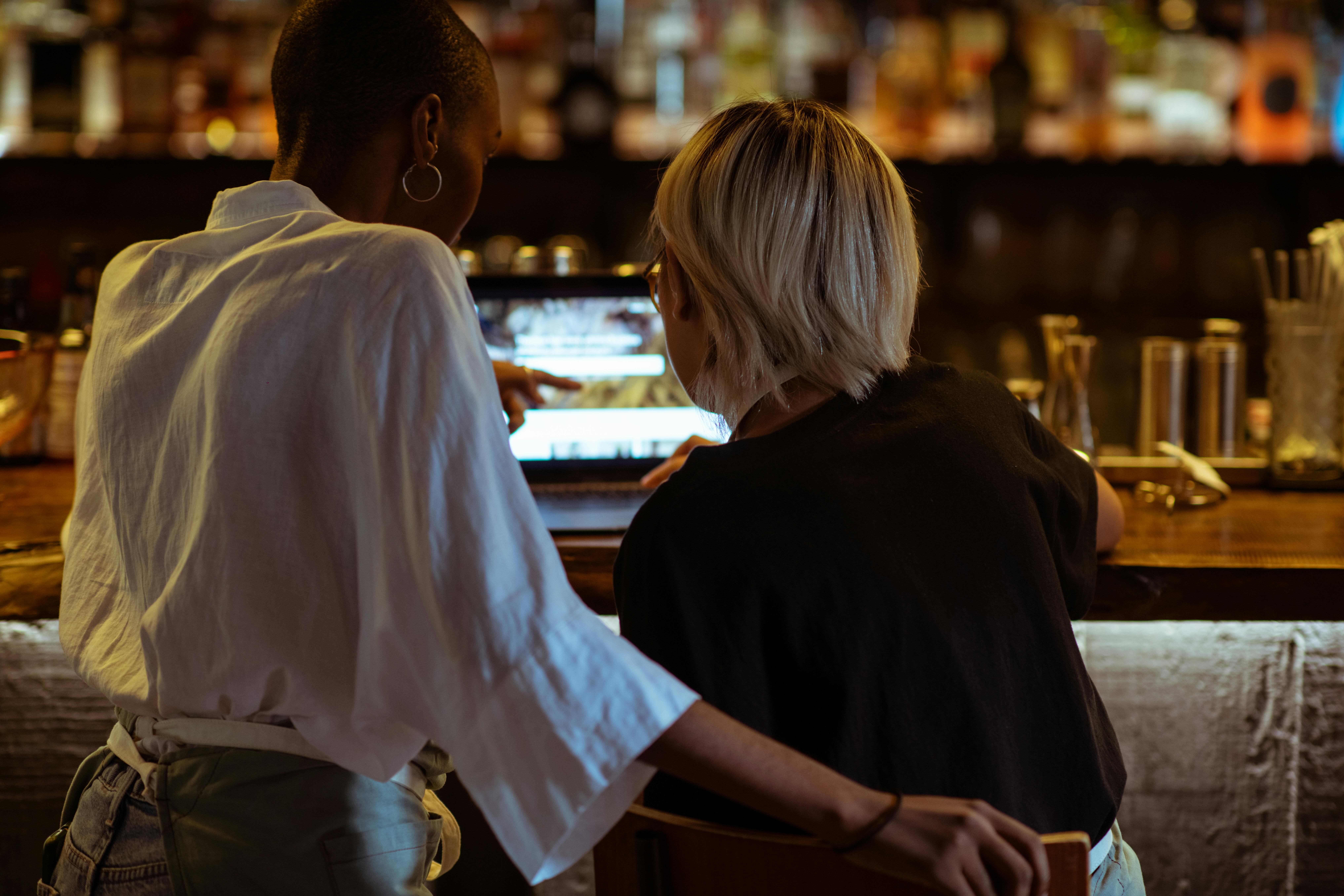 Mitarbeiterinnen arbeiten gemeinsam an einem Laptop in einem Restaurant